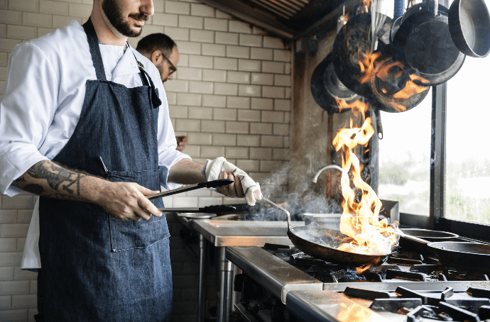 Chef cocinando con sartén en cocina profesional